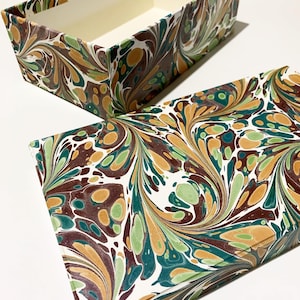 May include: A rectangular box with a marbled pattern in shades of green, brown, and orange. The box is open, revealing a white interior.