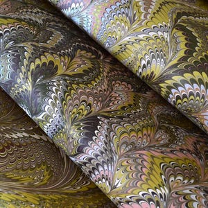 Pode incluir: Folhas de papel com um padrão marmoreado com formas repetitivas em leque em tons de verde-azeitona, castanho-escuro, branco e rosa suave. O design intrincado exibe linhas fluidas e rodopiantes que criam uma textura visual densa e em camadas.