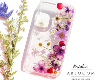 Könnte beinhalten: Eine transparente Handyhülle mit gepressten Blumen darin. Die Blumen sind in Rosa-, Lila- und Weißtönen. Der Text "Kristin ABLOOM FLORAL DESIGN" ist auf der Unterseite der Hülle aufgedruckt.