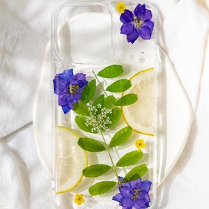 Puede incluir: Una funda transparente para tel&eacute;fono con flores prensadas y rodajas de lim&oacute;n. Las flores son moradas y amarillas. Esta funda incluye perlas. Nota 'sin perlas' en la caja si lo prefieres.