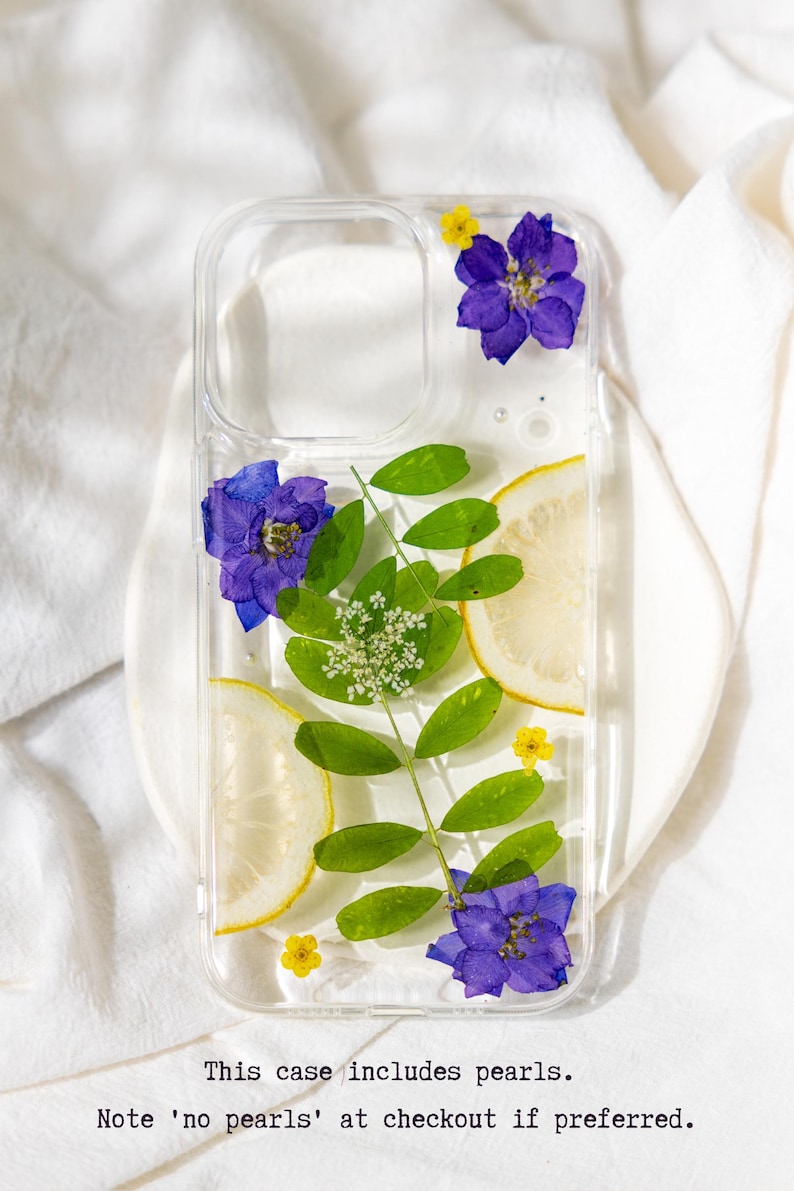 Puede incluir: Una funda transparente para tel&eacute;fono con flores prensadas y rodajas de lim&oacute;n. Las flores son moradas y amarillas. Esta funda incluye perlas. Nota 'sin perlas' en la caja si lo prefieres.