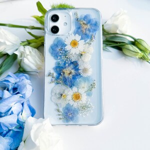 May include: A clear phone case with a design of pressed blue and white flowers. The case is on a white surface.