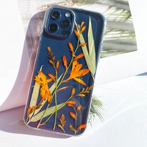 May include: A clear phone case with a black background and pressed orange flowers and green leaves.