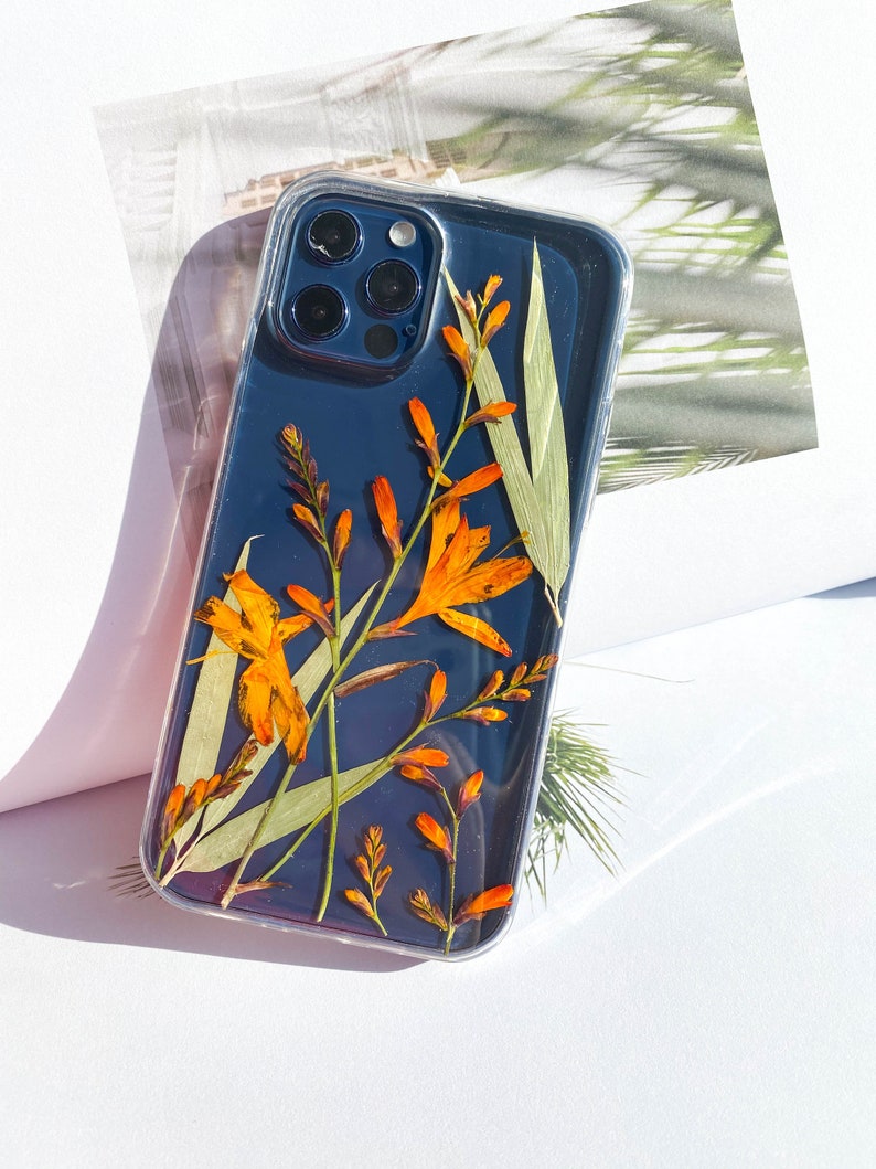 May include: A clear phone case with a black background and pressed orange flowers and green leaves.