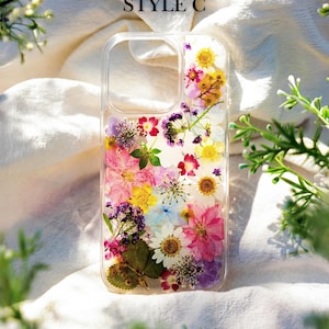 May include: A clear phone case with a pressed flower design. The case features a variety of colorful flowers, including pink, purple, yellow, and white. The case is labeled "STYLE C".