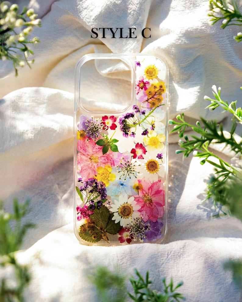 May include: A clear phone case with a pressed flower design. The case features a variety of colorful flowers, including pink, purple, yellow, and white. The case is labeled "STYLE C".