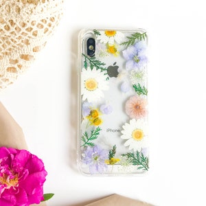 May include: A clear phone case with pressed flowers. The flowers are white, yellow, pink, and purple. The case has the word "iPhone" printed on it.