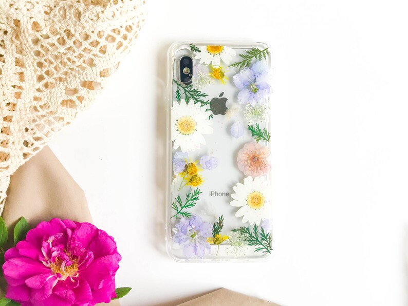 May include: A clear phone case with pressed flowers. The flowers are white, yellow, pink, and purple. The case has the word "iPhone" printed on it.