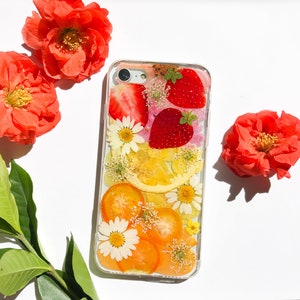 May include: A clear phone case with a pressed flower and fruit design. The case features strawberries, lemons, and orange slices, along with white and pink flowers.