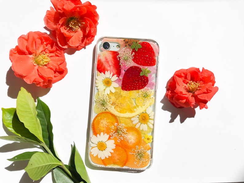 May include: A clear phone case with a pressed flower and fruit design. The case features strawberries, lemons, and orange slices, along with white and pink flowers.