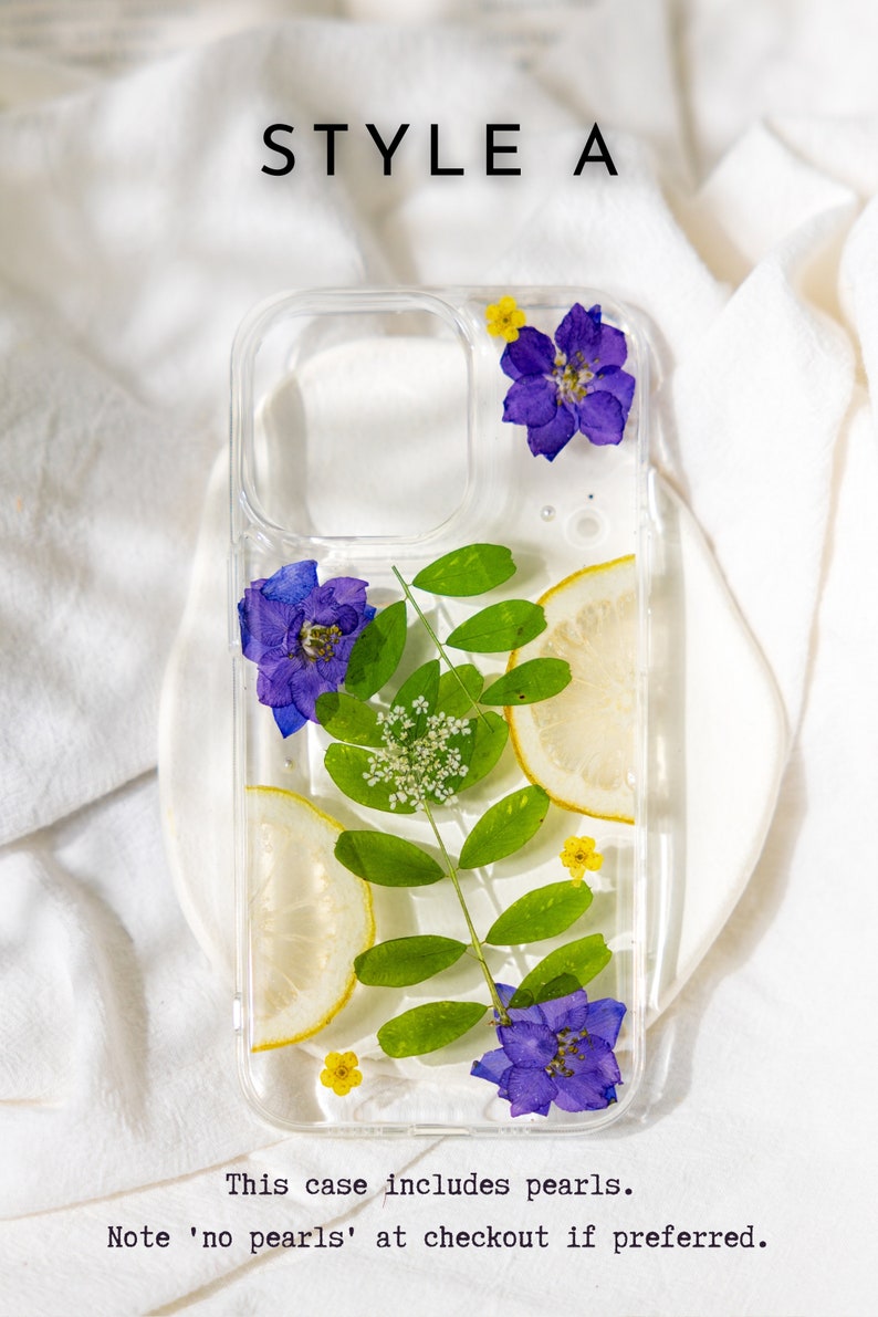 May include: A clear phone case with a pressed flower design. The case features purple flowers, green leaves, and a lemon slice. The text "STYLE A" is at the top of the image. The text "This case includes pearls. Note 'no pearls' at checkout if preferred." is at the bottom of the image.