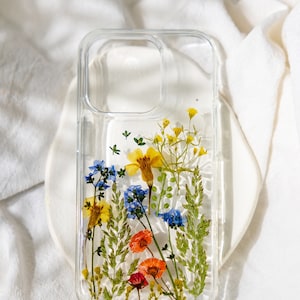 May include: A clear phone case with pressed flowers inside. The flowers are yellow, blue, orange, and red. The case has a raised lip around the camera lens.
