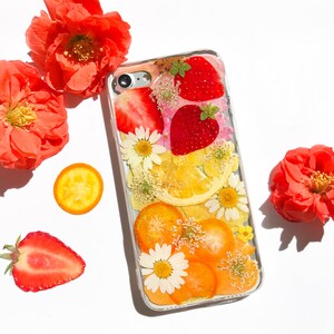 May include: A clear phone case with a pressed flower design featuring strawberries, lemons, and daisies. The case is decorated with dried fruit and flowers.