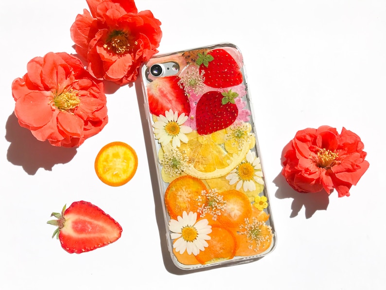 May include: A clear phone case with a pressed flower design featuring strawberries, lemons, and daisies. The case is decorated with dried fruit and flowers.