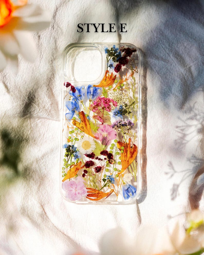 May include: A clear phone case with a pressed flower design. The case features a variety of flowers in shades of blue, pink, orange, and white. The text "STYLE E" is printed on the top of the case.