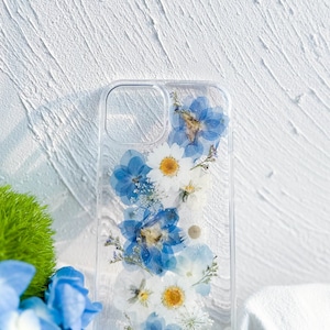 May include: A clear phone case with pressed blue and white flowers. The flowers are arranged vertically in a pattern.
