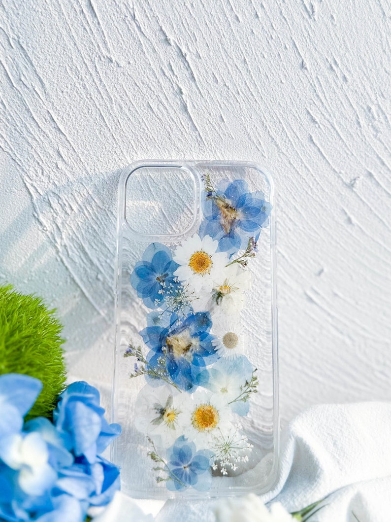 May include: A clear phone case with pressed blue and white flowers. The flowers are arranged vertically in a pattern.
