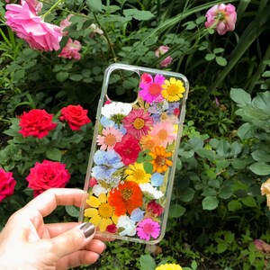 May include: A clear phone case with a pressed flower design. The case features a variety of colorful flowers, including pink, yellow, red, and white.