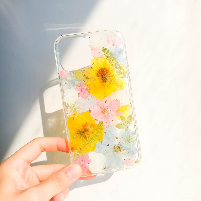 May include: A clear phone case with pressed flowers and gold glitter. The flowers are yellow, pink, and blue.