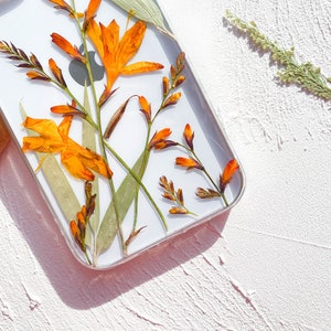May include: A clear phone case with pressed orange and yellow flowers. The flowers are pressed between the clear plastic and the white phone case.