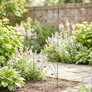 Puede incluir: Un enrejado de jardín de metal decorativo con un marco rectangular. El enrejado presenta un diseño de vid estilizado con hojas y pequeños pájaros. El metal tiene un acabado oscuro y envejecido, y el enrejado está en un jardín con flores.