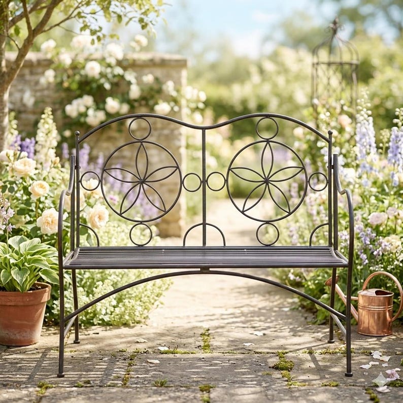 Puede incluir: Un banco de jard&iacute;n de metal marr&oacute;n oscuro con un dise&ntilde;o floral en el respaldo. El banco tiene un asiento curvo y est&aacute; rodeado de un exuberante jard&iacute;n con flores y vegetaci&oacute;n. El banco mide aproximadamente 122 cm de ancho.
