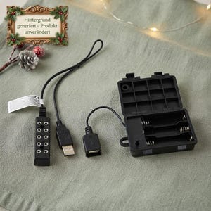 Op de afbeelding: Een zwarte plastic batterijhouder met een open scharnierend deksel, verbonden via een zwarte draad met een USB-A-connector en een kleine zwarte rechthoekige hub met meerdere ronde poorten. Een wit rechthoekig label met tekst is aan de draad bevestigd.
