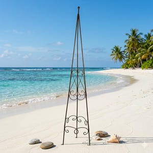 Pode incluir: Um obelisco de jardim alto, de metal castanho escuro, com volutas decorativas e um topo arredondado. O obelisco está numa praia arenosa com o oceano e palmeiras ao fundo. O obelisco tem aproximadamente 183 cm de altura.