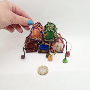 Pode incluir: Uma coleção de casas decorativas em miniatura e coloridas. Cada casa apresenta um esquema de cores único, incluindo laranja, verde e vermelho, com detalhes intrincados. Pequenos pingentes decorativos pendem de algumas casas. Uma moeda está em primeiro plano.