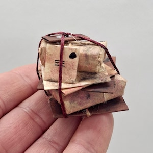 Può includere: Un mucchio di piccoli pacchetti marroni avvolti in carta, legati insieme da uno spago rosso. I pacchetti sono legati da uno spago rosso e hanno un'etichetta scritta a mano con inchiostro nero.