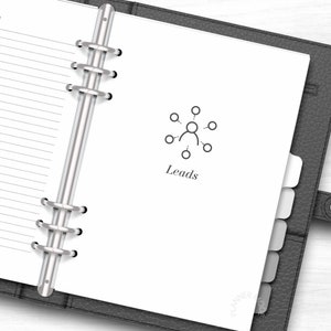 K&ouml;nnte beinhalten: Ein wei&szlig;er Planer mit einem silbernen Binder. Der Planer hat einen Registerkartenbereich und eine Seite mit einem grauen Symbol einer Person mit Linien, die Kreise um sie herum verbinden. Der Text "Leads" befindet sich unter dem Symbol.