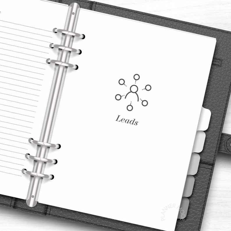 K&ouml;nnte beinhalten: Ein wei&szlig;er Planer mit einem silbernen Binder. Der Planer hat einen Registerkartenbereich und eine Seite mit einem grauen Symbol einer Person mit Linien, die Kreise um sie herum verbinden. Der Text "Leads" befindet sich unter dem Symbol.