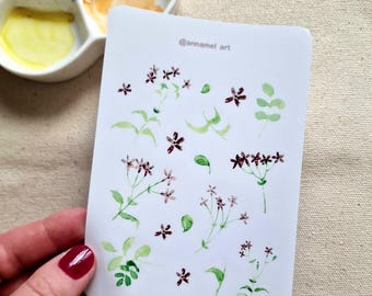Könnte beinhalten: Ein Bogen Aufkleber mit Aquarell-Illustrationen von kleinen lila Blüten und grünen Blättern. Die Aufkleber sind auf weißem Hintergrund und haben den Text "@annamel_art" in der oberen rechten Ecke.