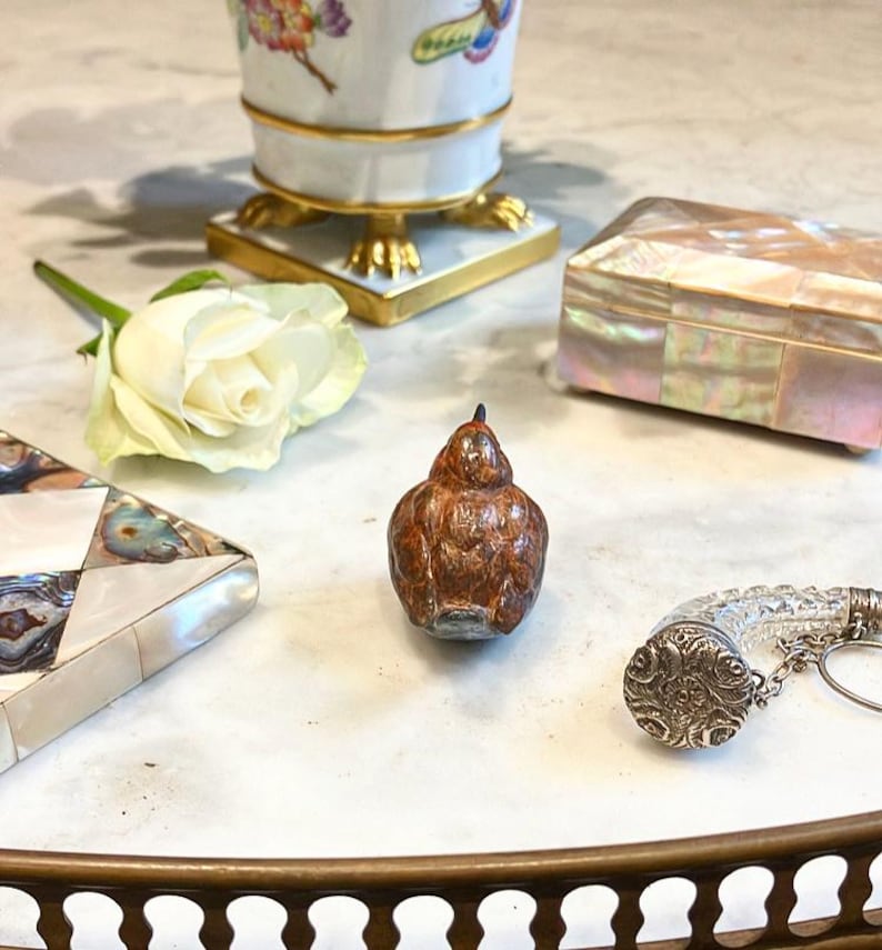 May include: A small, brown, ceramic bird figurine with a textured surface. The bird is sitting on a white marble surface.