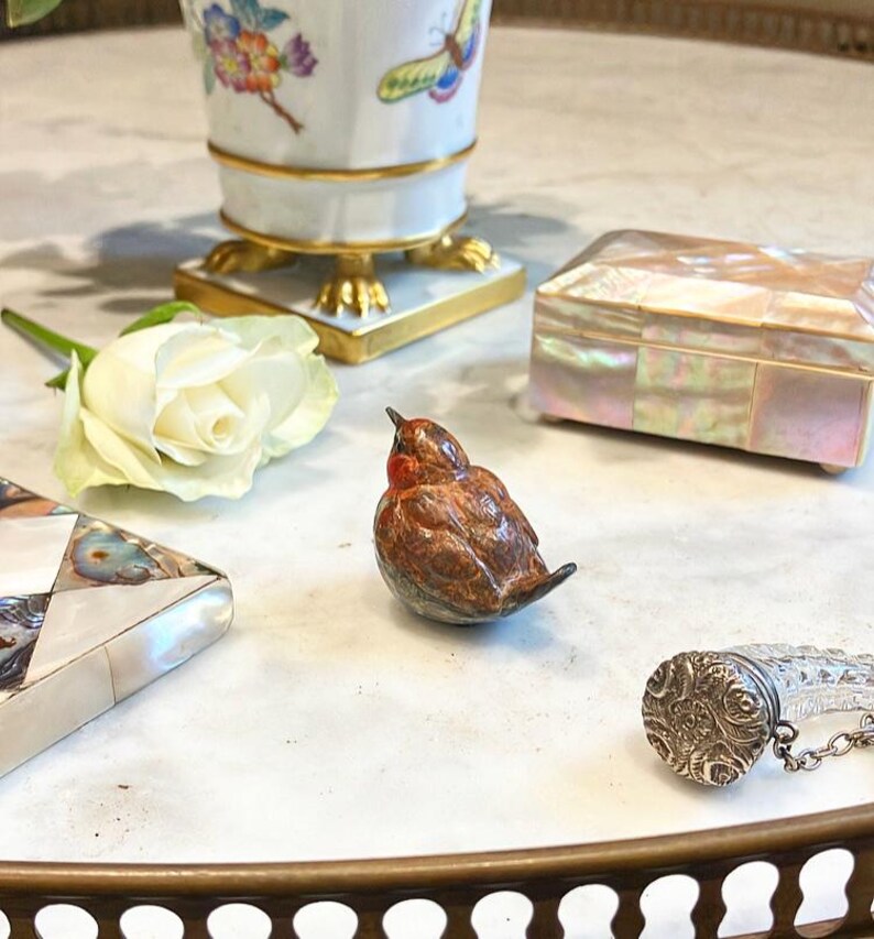 May include: A small, brown and red bird figurine with a white rose and a mother of pearl box on a marble surface.