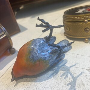 Puede incluir: Una peque&ntilde;a figurita de p&aacute;jaro de cer&aacute;mica con un esmalte azul y naranja. El p&aacute;jaro est&aacute; acostado de espaldas con las alas extendidas.