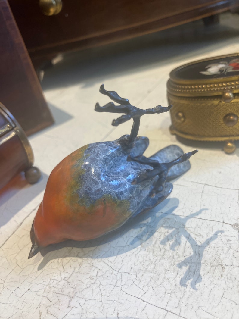 Puede incluir: Una peque&ntilde;a figurita de p&aacute;jaro de cer&aacute;mica con un esmalte azul y naranja. El p&aacute;jaro est&aacute; acostado de espaldas con las alas extendidas.