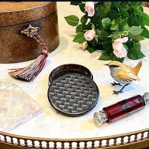May include: A brown wooden box with a gold latch and a red tassel, a black and silver round box with a woven lid, a white and iridescent mother of pearl box, a small brown bird figurine, and a red glass bottle with a silver stopper.