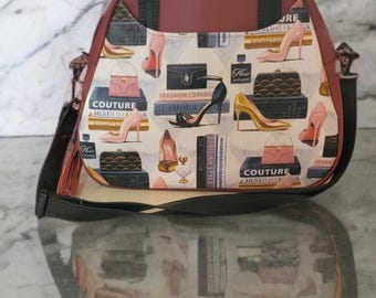 May include: A maroon leather tote bag with a black strap and a cream canvas lining. The lining features a print of high heels, purses, and books with the text "Couture Must Haves" and "Fashion Lookbook".