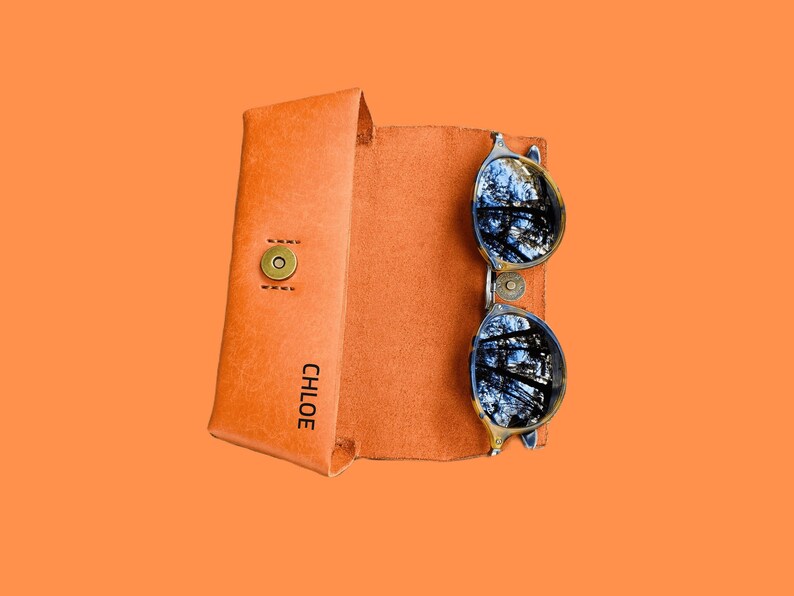 Puede incluir: Un estuche de gafas de sol de cuero marr&oacute;n con el nombre "CHLOE" grabado en la parte delantera. El estuche est&aacute; abierto y un par de gafas de sol redondas con lentes oscuras est&aacute;n dentro.