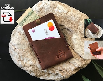 May include: Brown leather wallet with a single card slot and a small pocket. The wallet has a logo that says "ahoy" and a snap closure. The wallet is sitting on a rock.