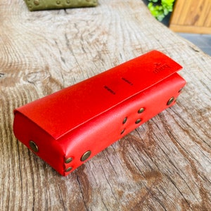 Puede incluir: Una funda de cuero roja con cierre de solapa y la palabra "ahoy" grabada en la parte delantera. La funda tiene remaches decorativos de lat&oacute;n alrededor de los bordes.
