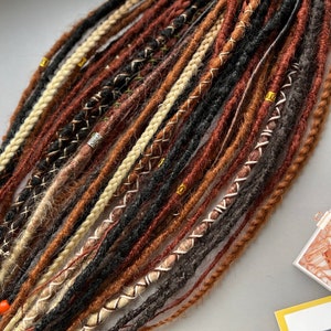 May include: A set of brown, black, and blonde synthetic dreadlocks with gold and silver beads. The dreadlocks are arranged in a fan shape and are ready to be installed.