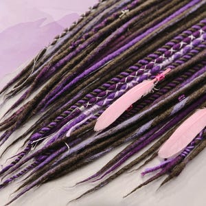 May include: A set of brown and purple synthetic dreadlocks with pink feathers. The dreadlocks are made of wool and have a variety of textures.