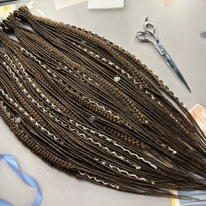 May include: A set of brown synthetic dreadlocks with white stitching and silver beads. The dreadlocks are arranged in a fan shape and are ready to be installed.