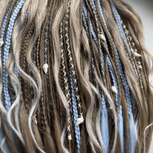 A close-up view of a person's long, braided hairstyle with various colored braids and small white or light blue beads or accessories.