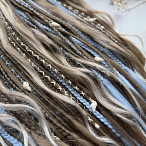 a close-up view of a collection of braided hair strands in various shades of brown and blue, with small white shells or beads interspersed throughout the braids.