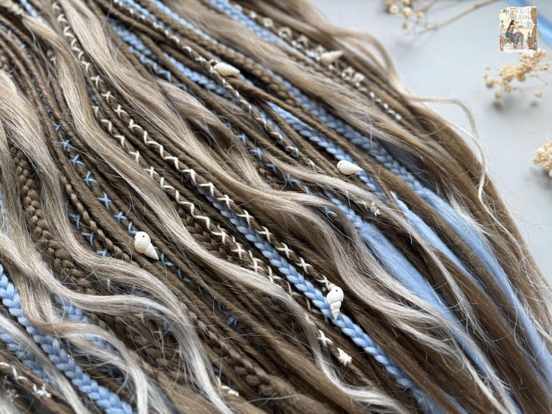 a close-up view of a collection of braided hair strands in various shades of brown and blue, with small white shells or beads interspersed throughout the braids.
