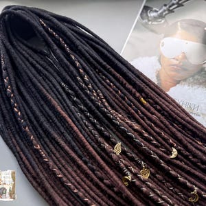 a collection of long, dark brown braided hair strands with various decorative elements such as beads and charms, as well as a magazine featuring a woman's face.