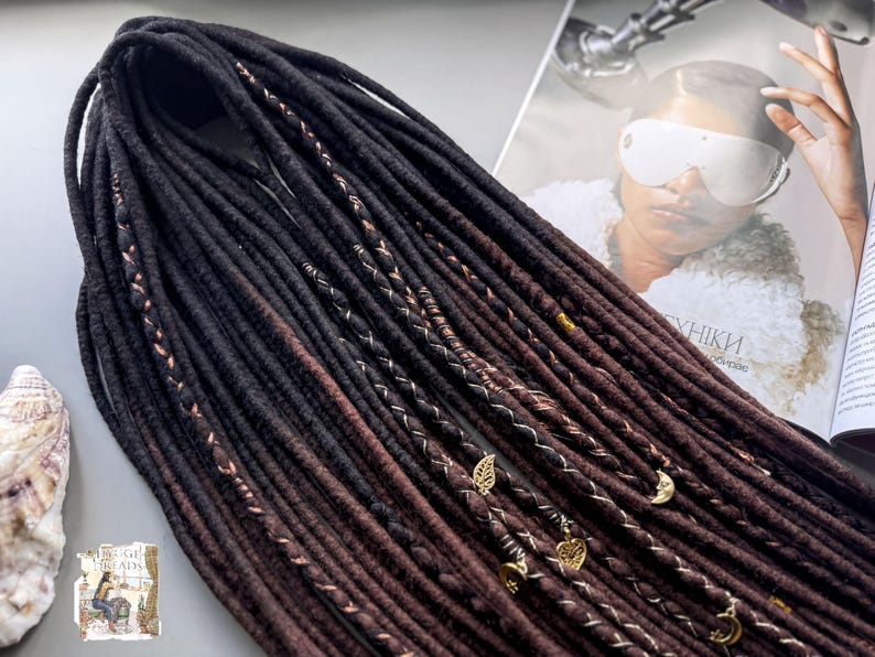 a collection of long, dark brown braided hair strands with various decorative elements such as beads and charms, as well as a magazine featuring a woman's face.
